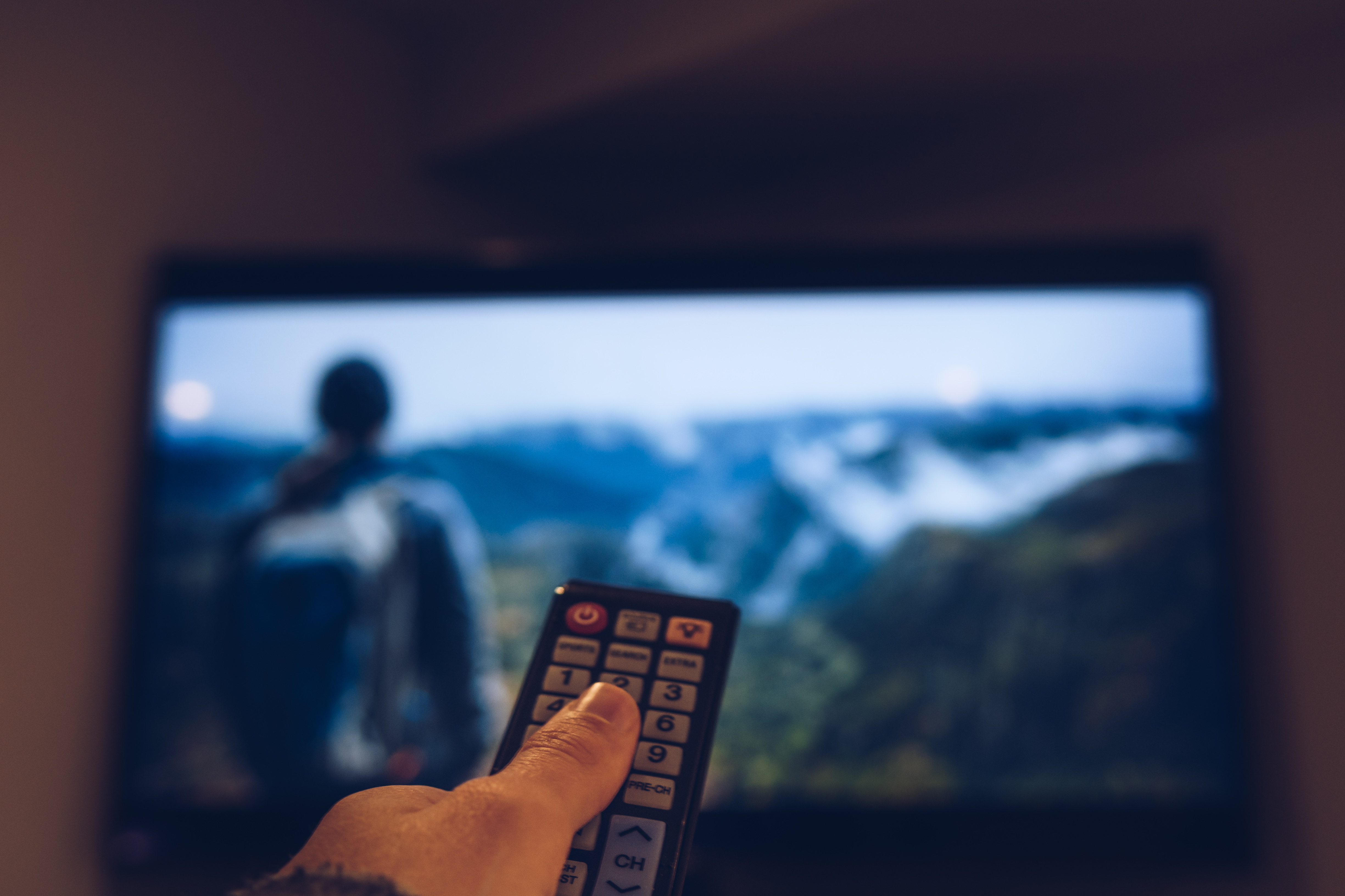 Cropped Image Of Hand Holding Remote Control In Front Of Television Set