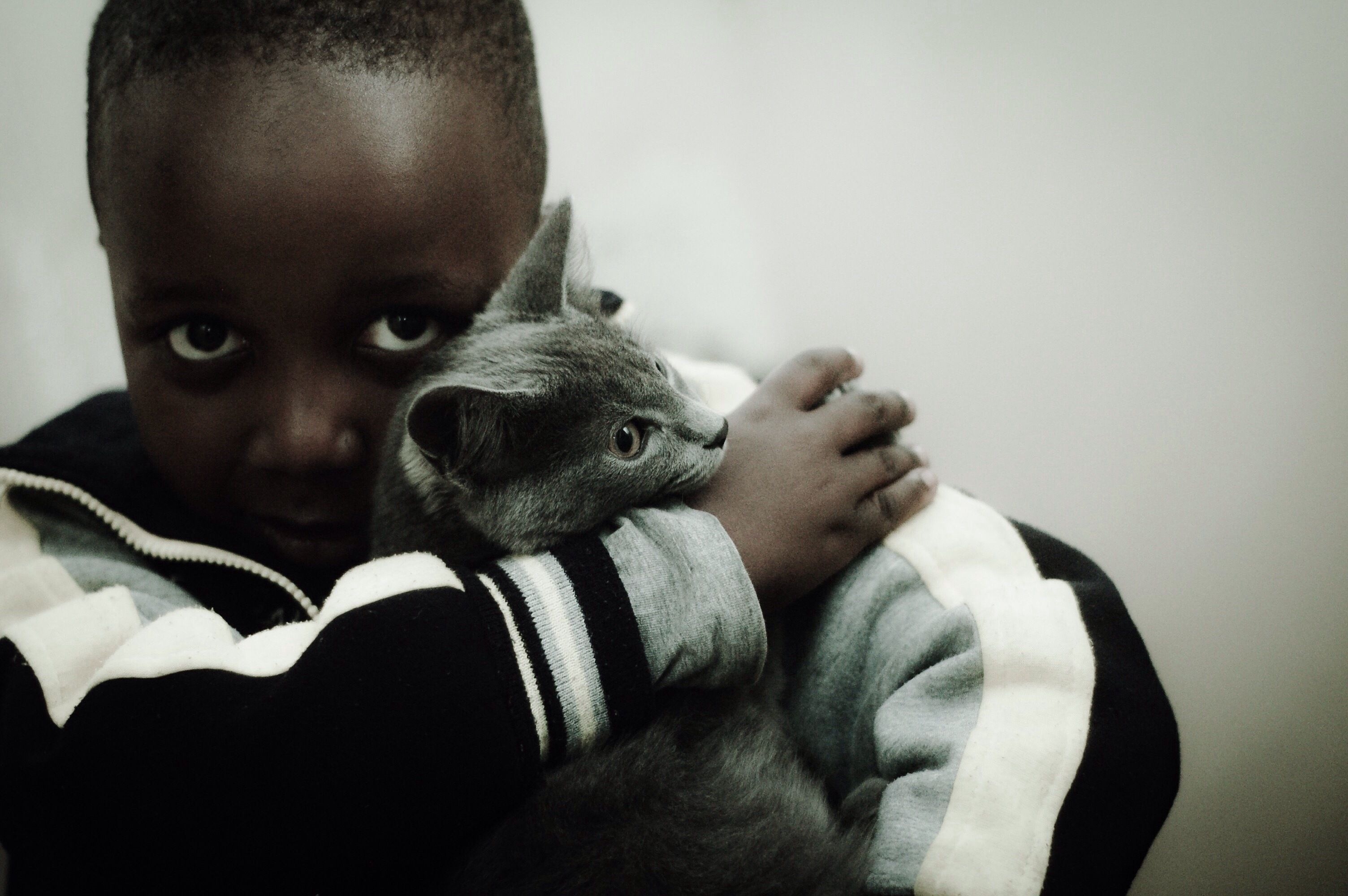 Portrait Of Boy Embracing Cat While Sitting Against Wall