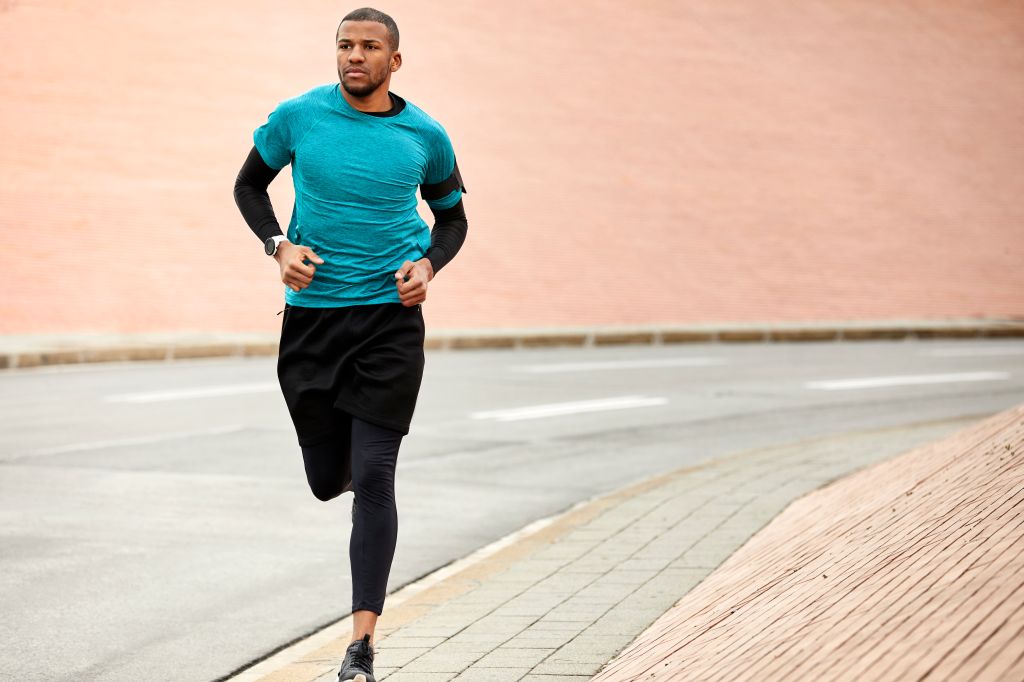 Young man jogging on roadside against wall in city