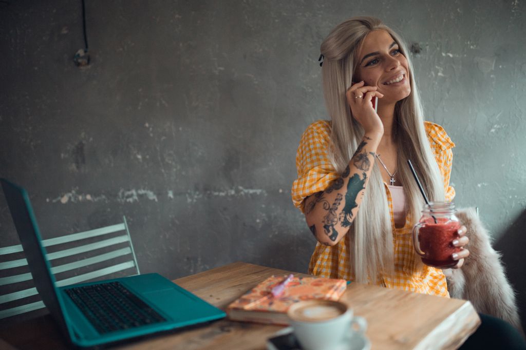Smiling young woman using phone inside the coffee bar