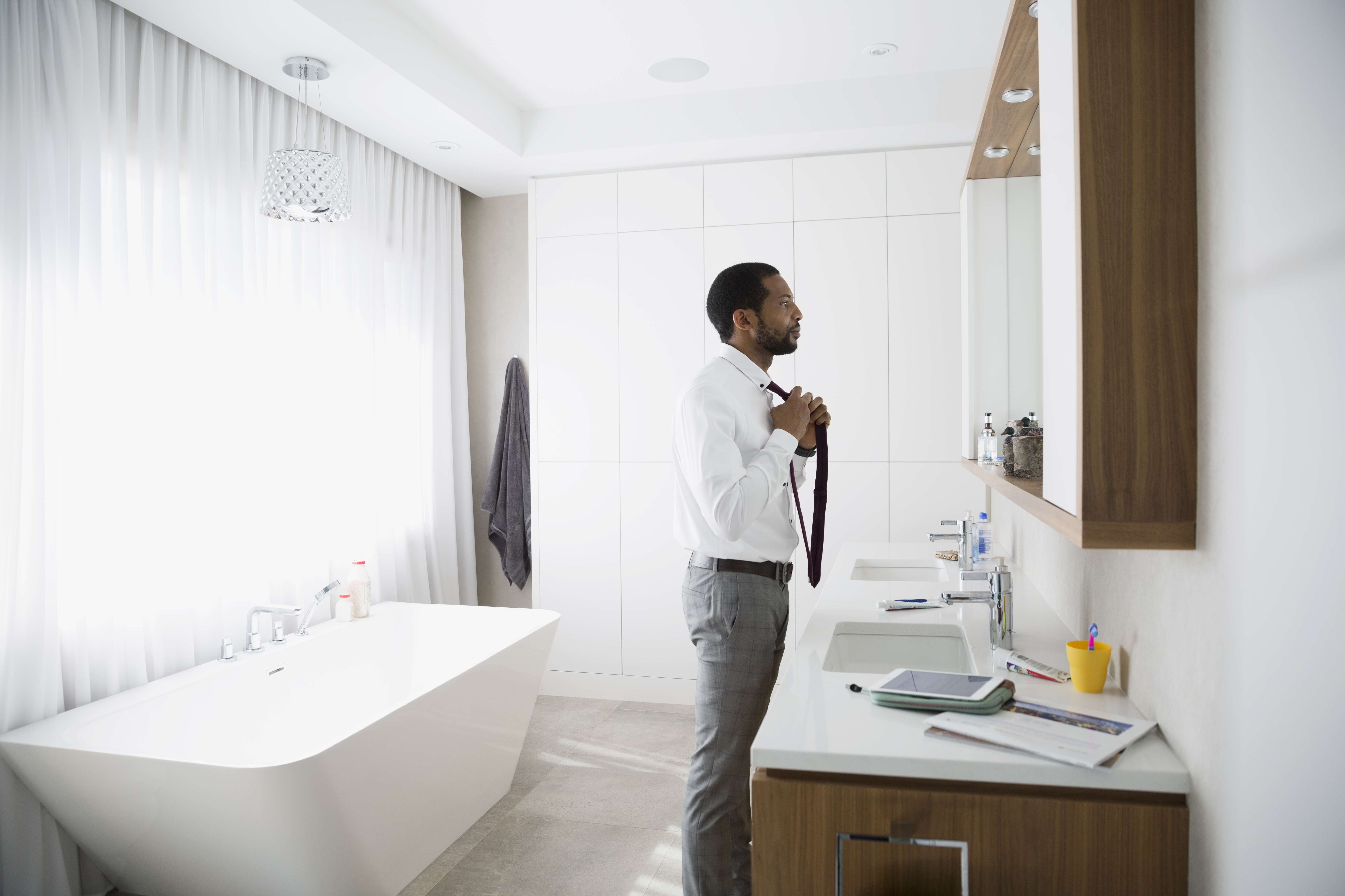 Man putting on tie at mirror in morning bathroom
