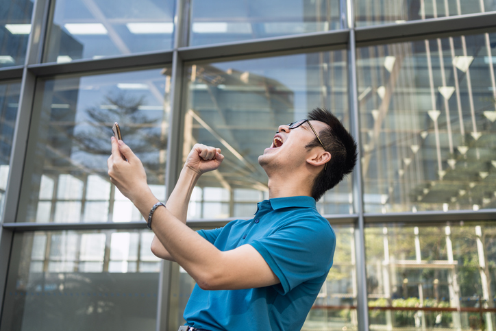 Excited Young Man cheering While Holding Mobile Phone