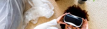 Afro woman wearing virtual reality simulator while lying on carpet in new apartment