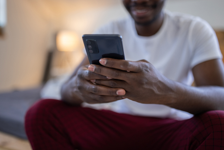 Young man text messaging while sitting on bed at home