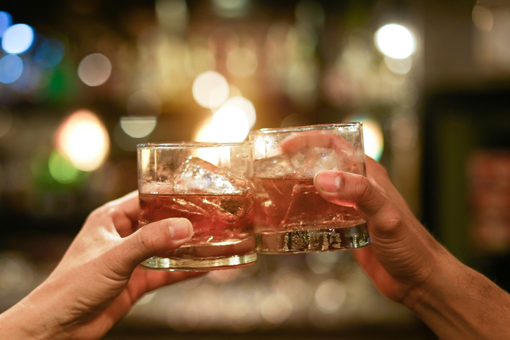 two men clinking glasses of whiskey drink alcohol beverage together at counter in the pub