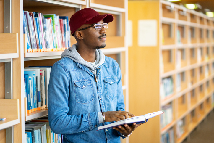 Portrait of a young Afro-American student n the library holding a book in the library