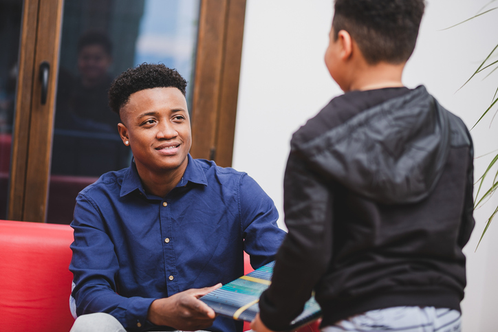 African american son giving gift his smiling father in living room.