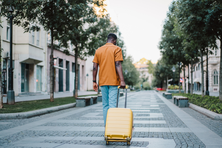 Rear view of young man walking through the city with suitcase.