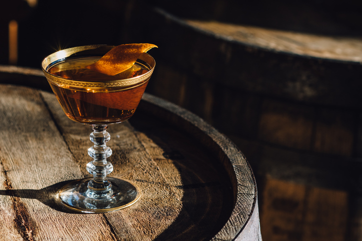 Manhattan Bourbon Whiskey Cocktail In Vintage Crystal Hotel Glass Orange Garnish Atop Wood Barrel