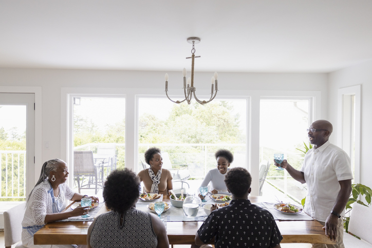 Senior man toasting family eating dinner together at dining table