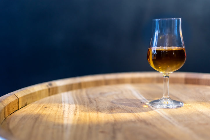 Glass of rum on oak cask close-up on blurred dark background