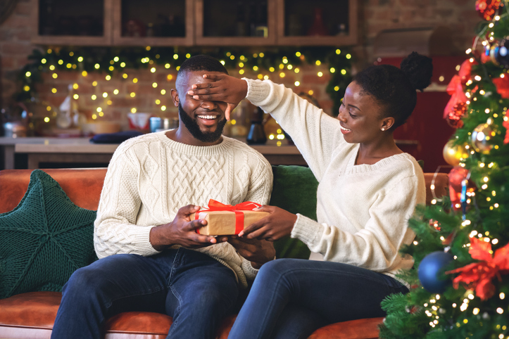 Wife presenting gift to husband in front of Christmas tree