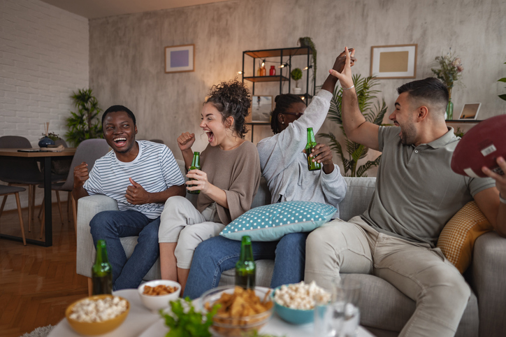 A lively gathering of friends cheering and enjoying snacks while watching a game on a cozy evening in a stylish living room setting