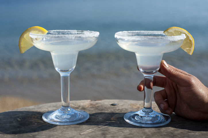 Men hand holding glass with margarita cocktail by the sea