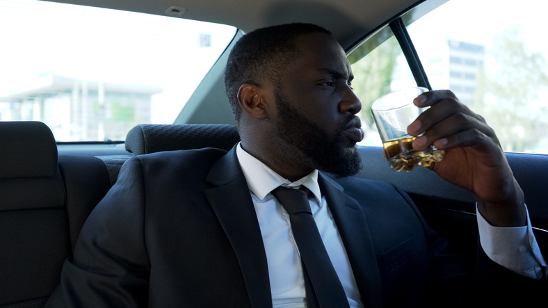 Self-confident rich man drinking alcohol in car, luxury lifestyle, success