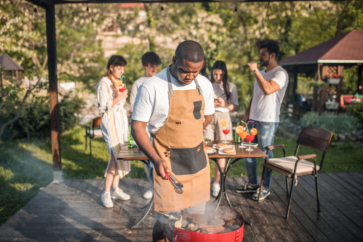 A black young man makes a barbecue in the yard for a group of his friends