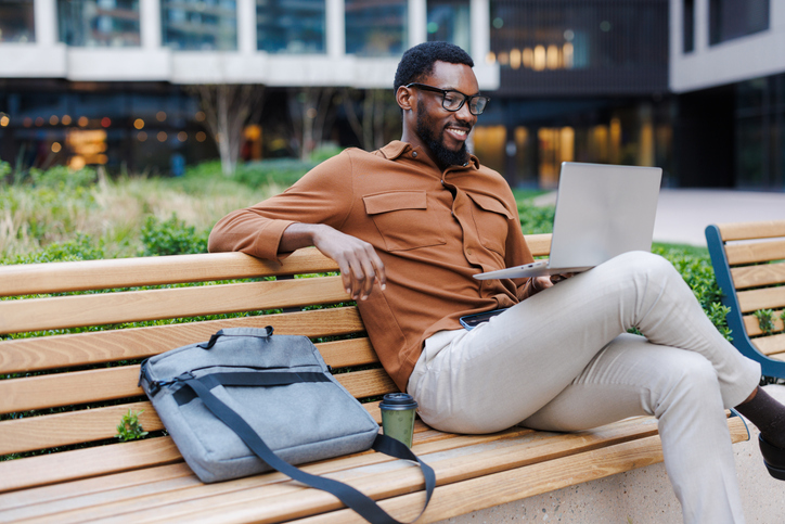 Man working on a laptop while sitting outdoors on a park bench