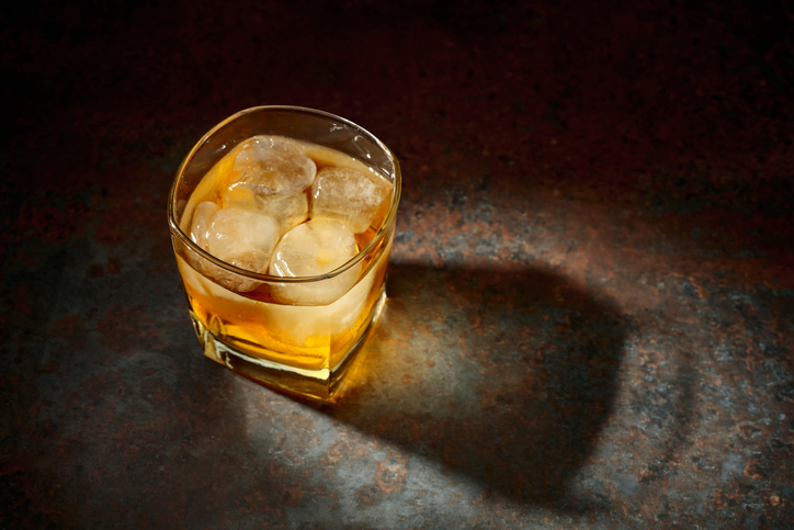 Whiskey in a square glass with ice on a vintage background.