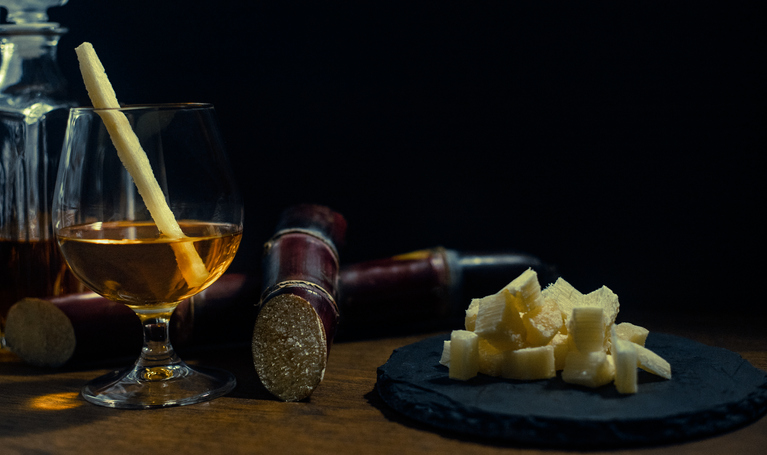 Glass of cane rum with pieces of cane on rustic wooden table and dark background