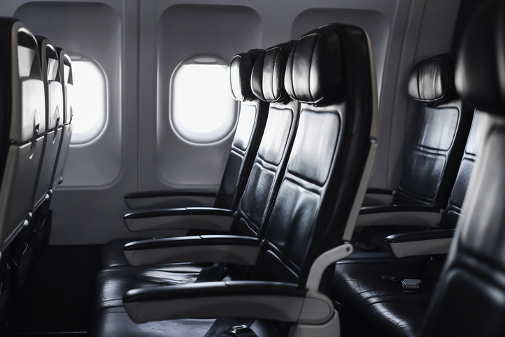 Empty airplane seats in passenger cabin. Leather chairs row inside modern aircraft interior. Bright light from window during flight.