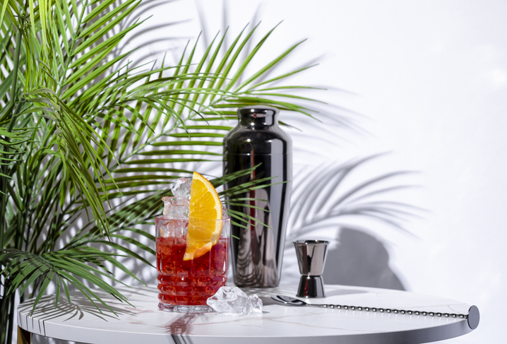 Mezcal negroni, alcoholic cocktail drink with red bitters, vermouth, ice and orange with bar tools