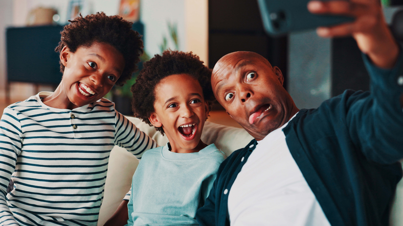 Selfie, funny face and dad with children on sofa for social media, profile picture and online post in home. Happy family, silly and father with kids take photo for bonding, fun and goofy together